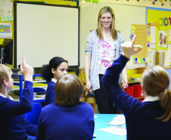 Teacher in a classroom with students raising their hands.