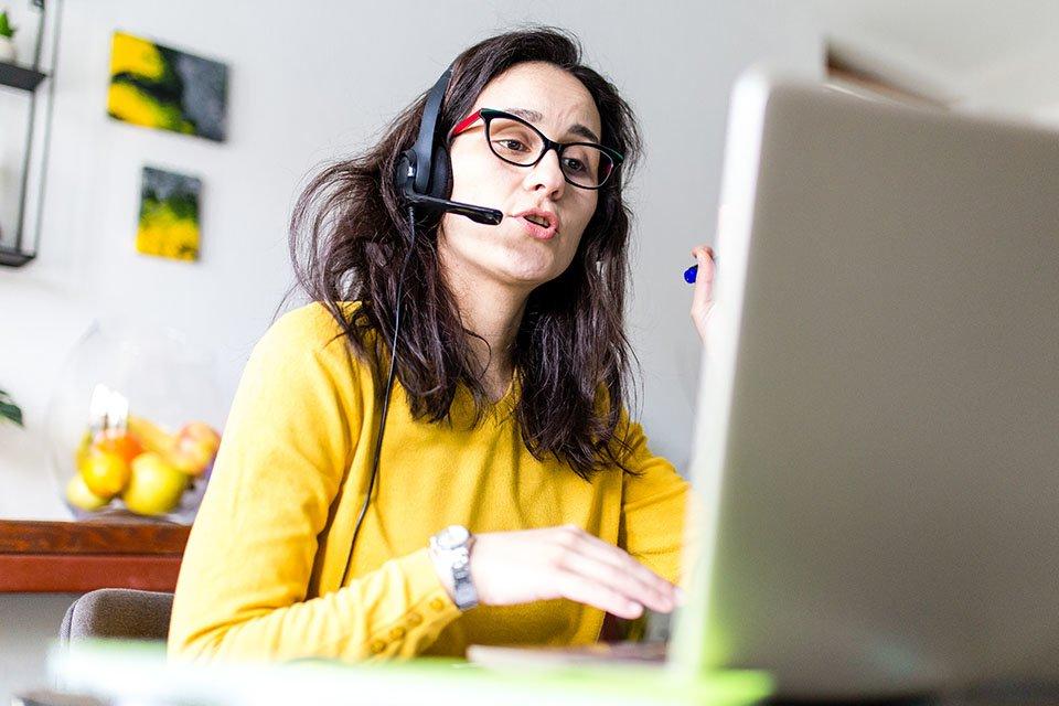 Woman with glasses working on computer and talking on headset.